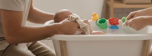 Papa donnant le bain à son bébé dans une baignoire bébé sécurisée, avec des jouets de bain
