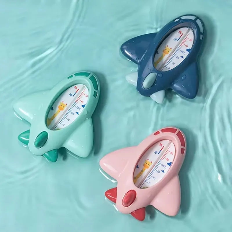 Comparaison de thermomètres de bain bébé avion analogiques en différentes couleurs, flottant à la surface de l’eau.